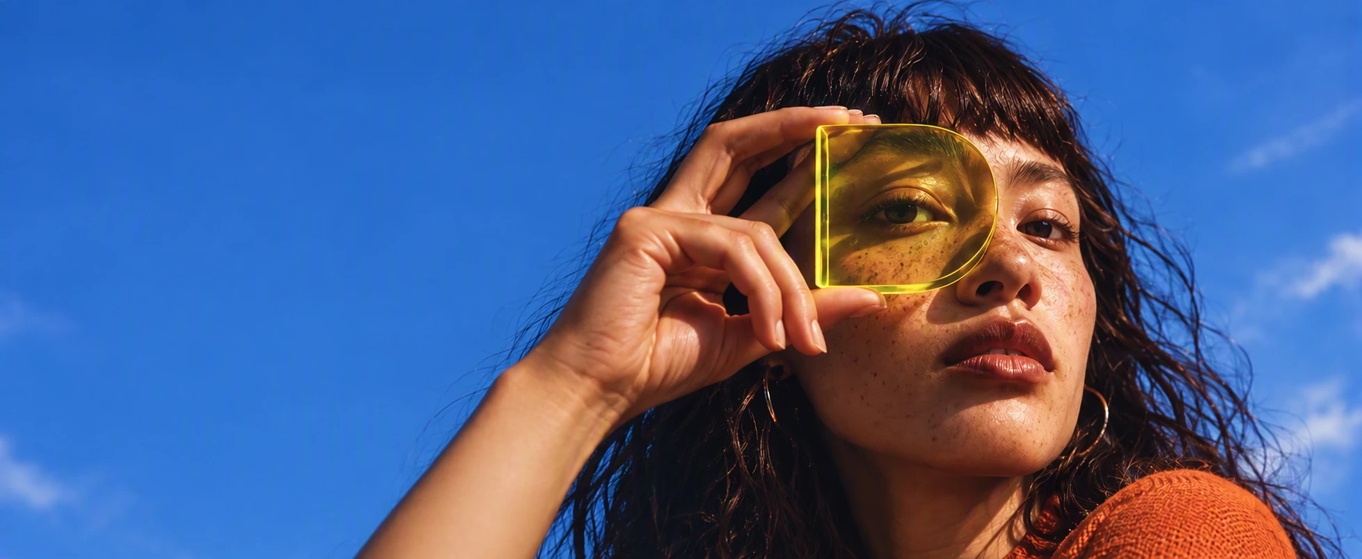 A woman looking through a yellow D-shaped lens against a blue sky